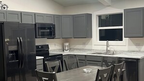 Una cocina moderna con armarios grises, un refrigerador negro, microondas, cafetera y una mesa de comedor con sillas.