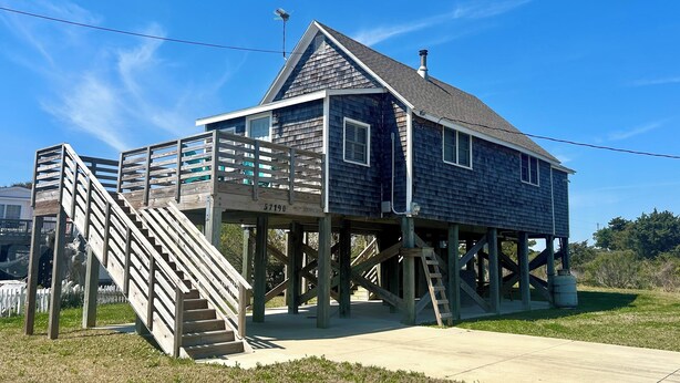 A wooden house with a balcony and stairs, number 57190, under a clear blue sky. - Cozy cottage in Hatteras Village. Convenient to shopping, restaurants and beach. (Hatteras)