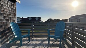 A wooden deck with two blue Adirondack chairs, a wooden fence, and houses in the background. - Cozy cottage in Hatteras Village. Convenient to shopping, restaurants and beach. (Hatteras)