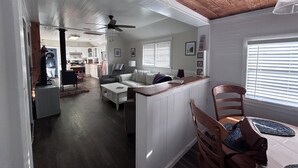 A spacious living area with a kitchen in the background, a dining area with a table and chairs, and a ceiling fan. - Cozy cottage in Hatteras Village. Convenient to shopping, restaurants and beach. (Hatteras)