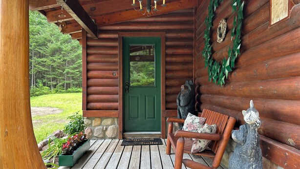 A wooden cabin with a green door, a bench, and a stone wall.