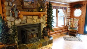 A cozy log cabin interior with a stone fireplace, wooden walls, and a rustic decor including a bear figurine and a Christmas tree.