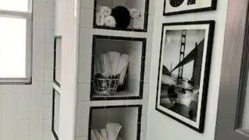 A bathroom with white tiled walls, a bathtub, and a shelf unit with various items.