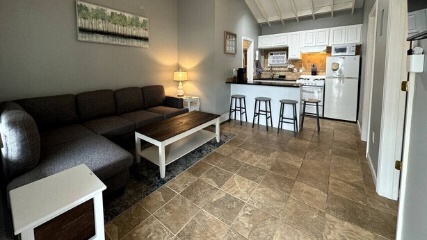 Una sala de estar moderna con un sofá, una mesa de centro y una zona de cocina con estufa, microondas y taburetes de bar.