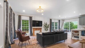 Un salon spacieux avec un canapé noir, un fauteuil en cuir marron, un téléviseur et une cheminée.