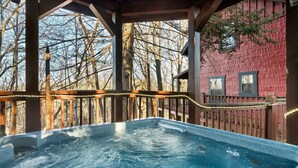 A hot tub under a wooden pergola with a view of a red building and leafless trees. - Cozy Cabin w/ 2 King Beds, Fireplace, Hot Tub, Foosball, Arcade and BBQ! (Sevierville)