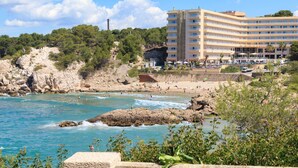 Un hôtel situé sur la côte, doté de nombreux balcons, d’une plage et de falaises rocheuses.