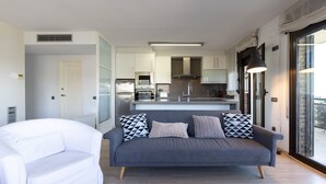 Un salon moderne avec un canapé gris, un fauteuil blanc et une cuisine en arrière-plan.