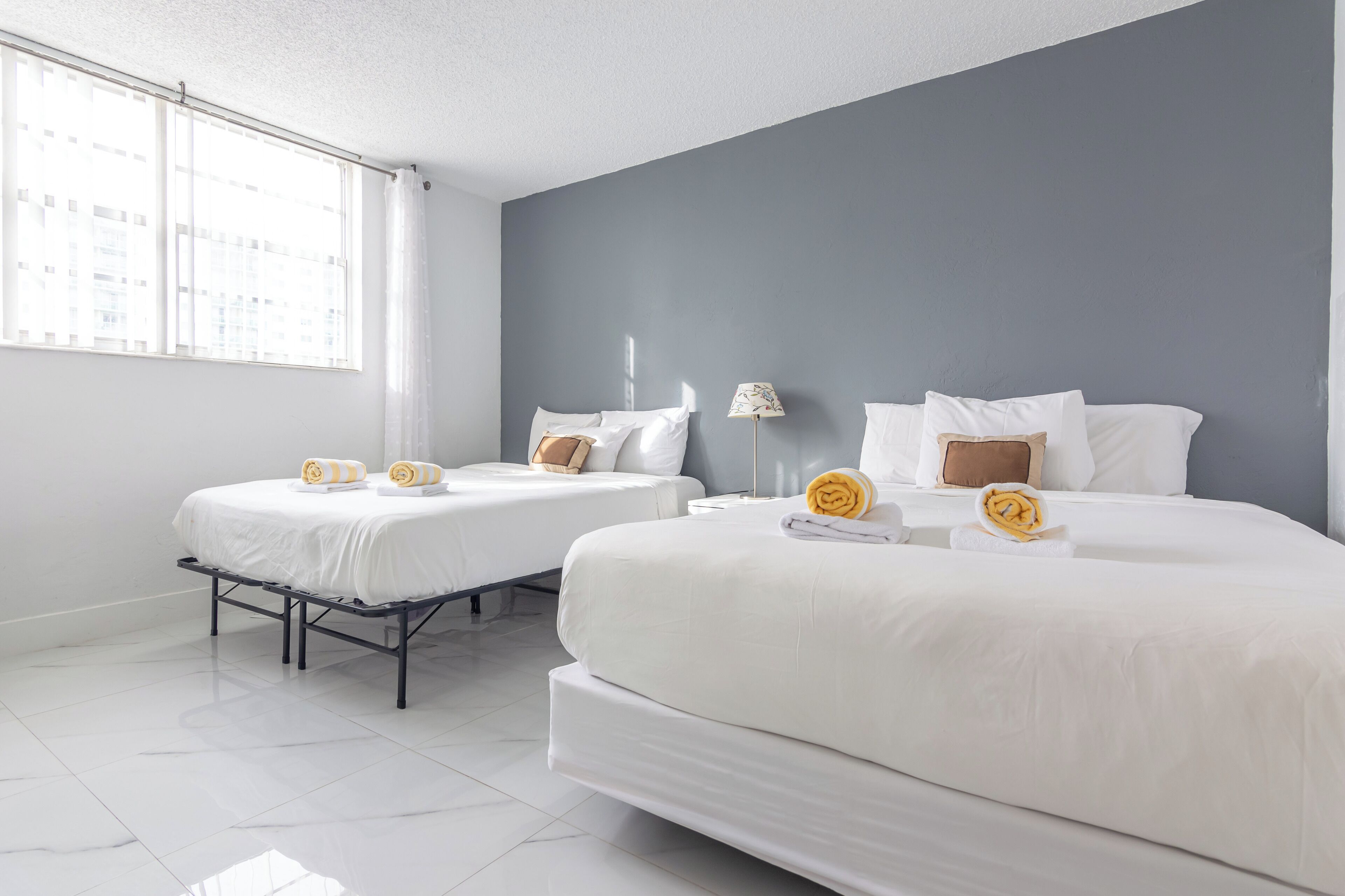 A hotel room with two beds, white bedding, and a grey accent wall.