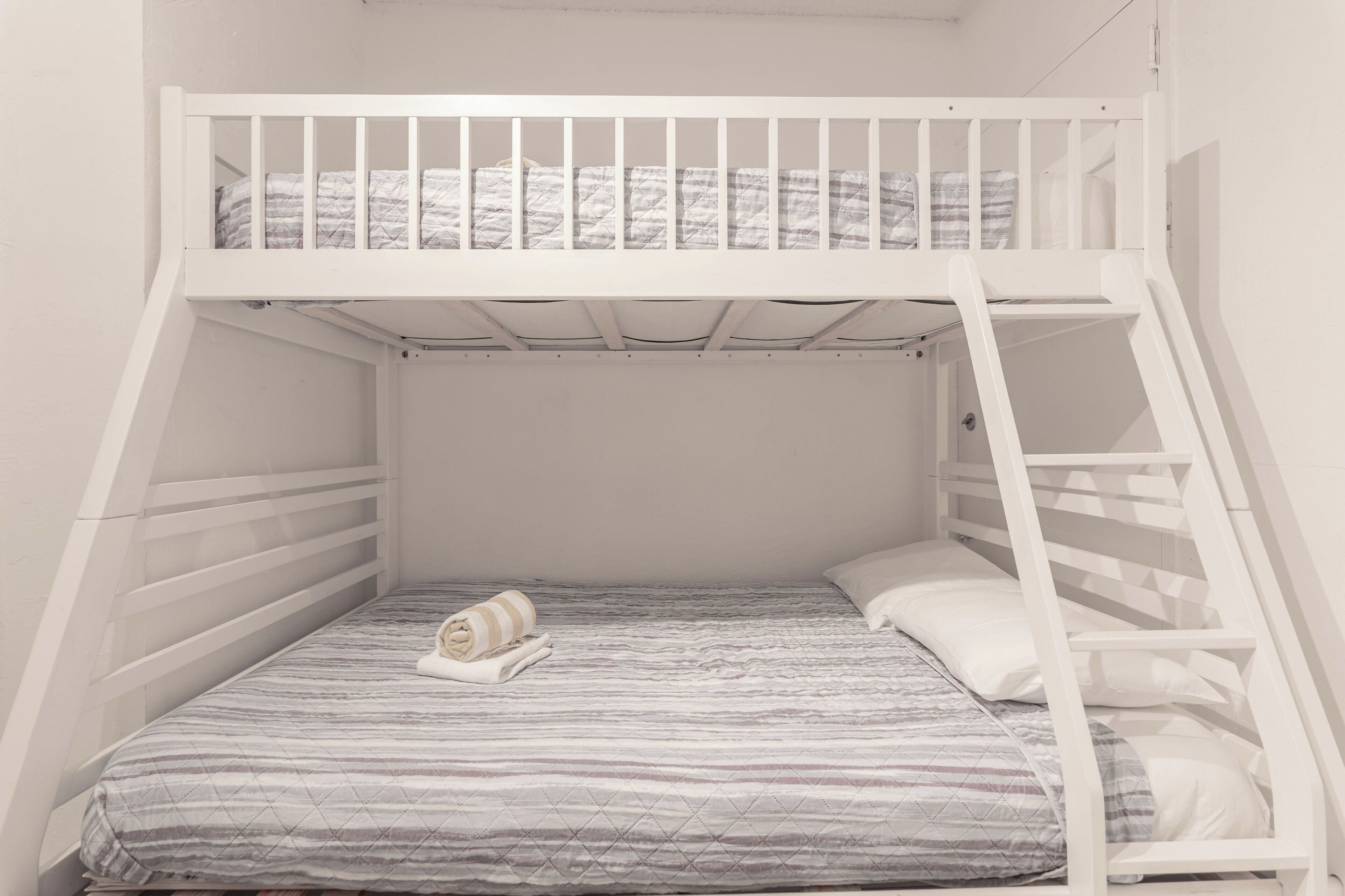 Ein Etagenbett mit einer Leiter, einer gestreiften Matratze und einem zusammengerollten Handtuch auf dem unteren Bett.