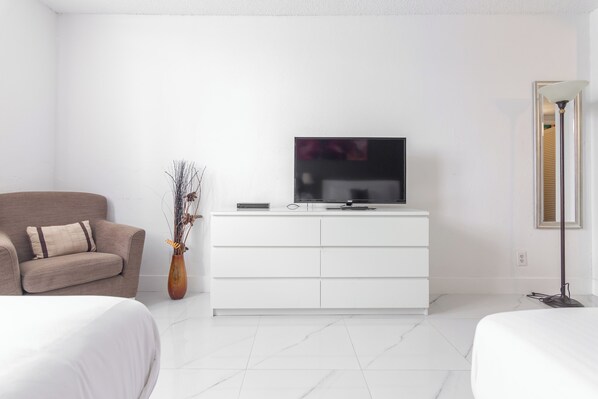 A modern hotel room with a white sofa, a TV on a white dresser, and a vase with branches. - Ocean Reserve by Boutique Apartments MIA (Sunny Isles Beach)