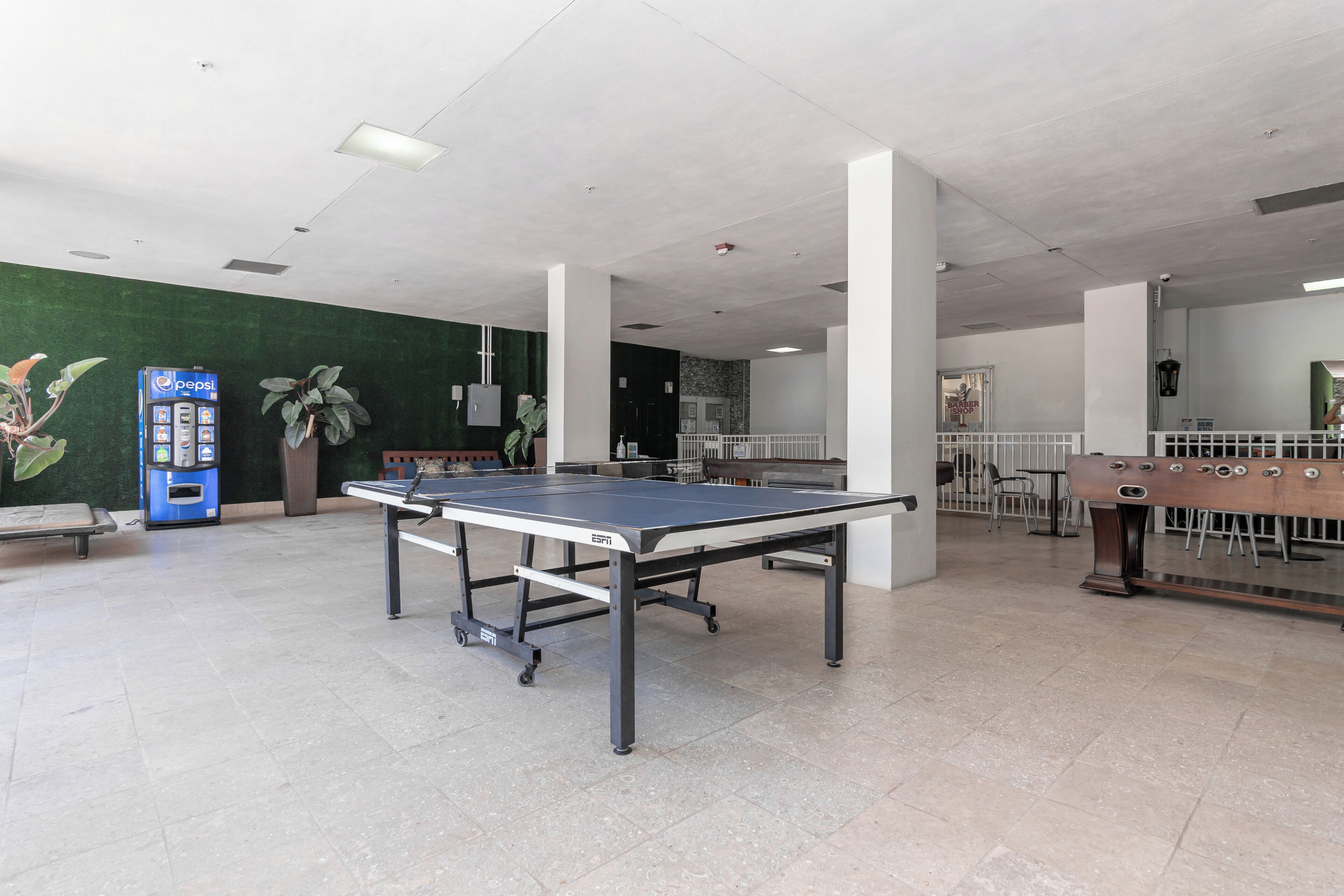 A spacious indoor area with a ping pong table, a foosball table, and a vending machine.