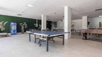 A spacious indoor area with a ping pong table, a foosball table, and a vending machine.
