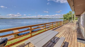 Una terraza de madera con barandilla que da a un lago, una mesa de picnic y un área cubierta con sillas.