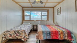 Una habitación con dos camas individuales, un ventilador de techo, una ventana con vistas y un cuadro en la pared.