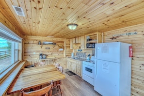 A wooden cabin interior with a kitchen area, including a dining table, chairs, a refrigerator, a stove, and a microwave. - Cabin on the Lake w/ 6-Beds - Open for Hunting/Rifle Season - Pets Ok (Gordon)