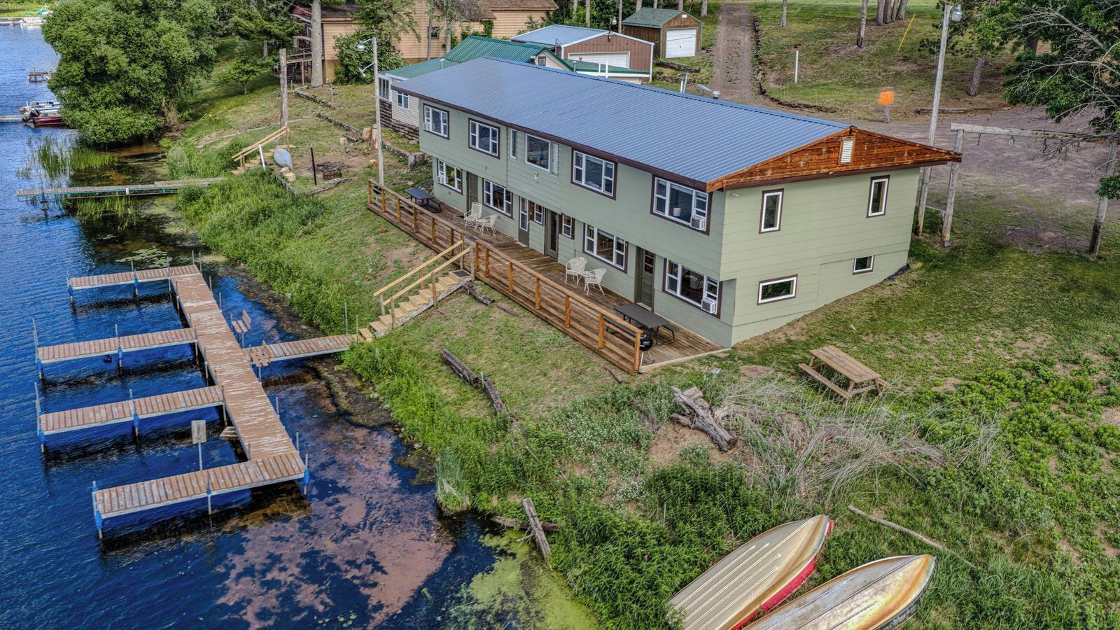 Uma casa de dois andares com um cais que se projeta sobre a água, rodeada por vegetação.