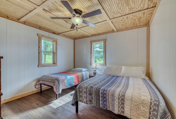 Ein Zimmer mit zwei Betten, einem Deckenventilator und Fenstern.