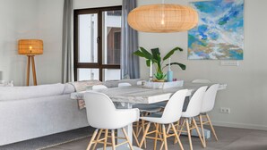 Et moderne spiseområde med et hvidt bord, hvide stole og et hængende rattanlys.