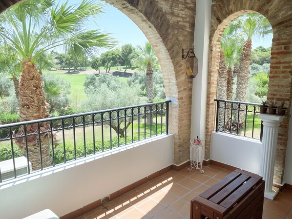 A balcony with a view of a garden, featuring palm trees and a brick wall.