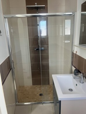 Une salle de bain moderne avec une douche en verre, un lavabo blanc et un miroir au-dessus du lavabo.