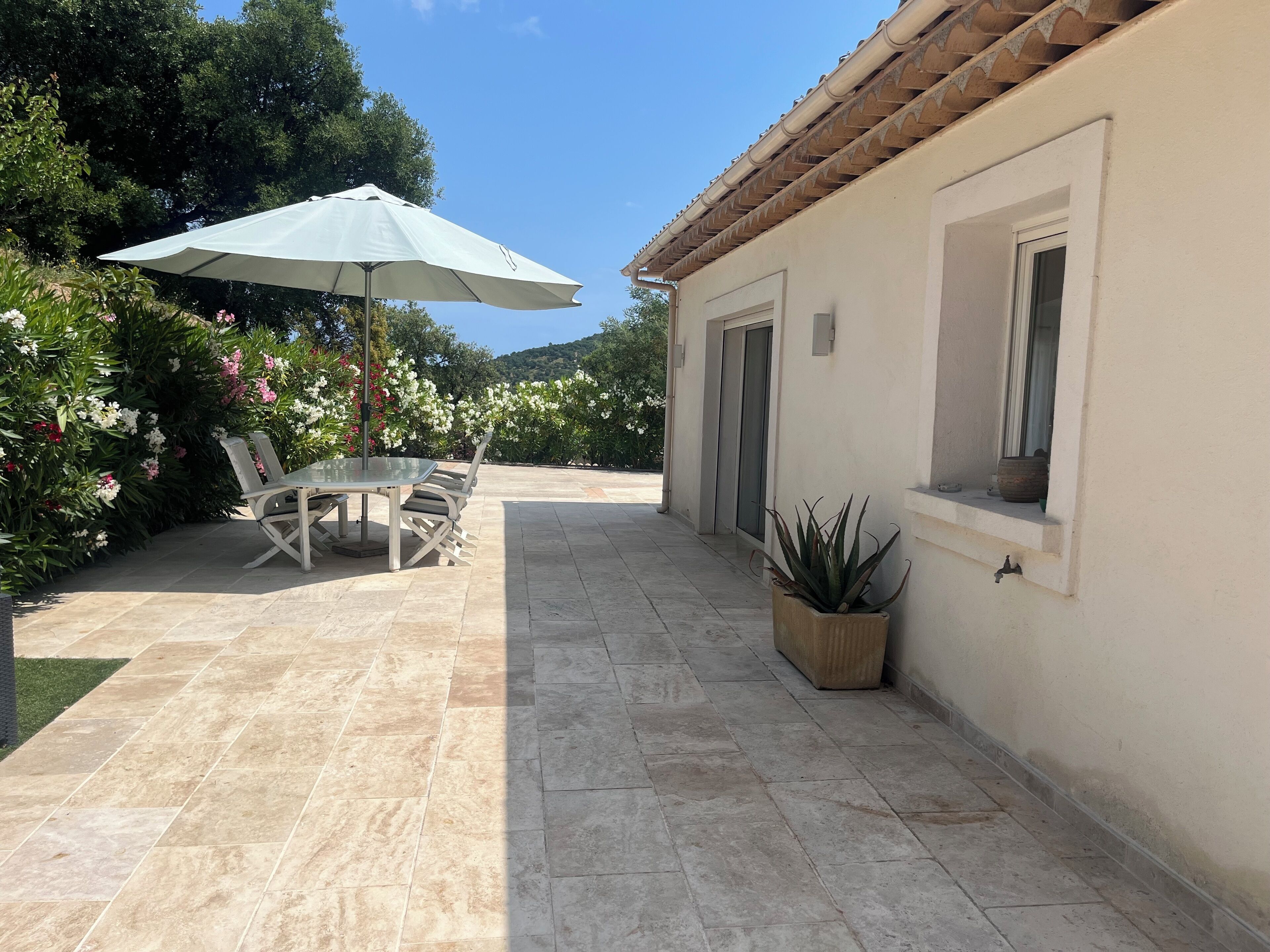 Une terrasse avec une table et des chaises, un pot de fleurs et un sol carrelé.