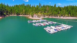An aerial view of a marina surrounded by dense forest, with boats docked and a clear sky above.