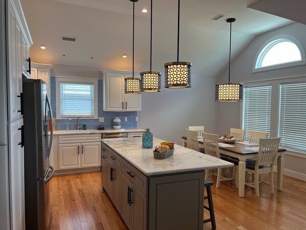 A modern kitchen with a central island, pendant lights, and a dining area with a table and chairs.