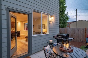 Eine Terrasse mit Grill, Sitzgelegenheiten im Freien und einer Glastür zum Essbereich im Innenbereich.