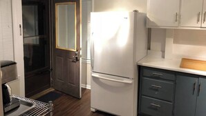 A compact kitchen with a refrigerator, cabinets, and a door leading to a dark room. - Spacious 1BR - Great Location @ Grandview & OSU! (Columbus)