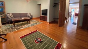 A spacious living room with hardwood flooring, a sofa, a coffee table, a TV, and a chandelier. - Clintonville Charmer | Walk to Great Restaurants! (Columbus)