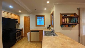 A kitchen with wooden cabinets, a black refrigerator, a dishwasher, and a large island with a sink. - Clintonville Charmer | Walk to Great Restaurants! (Columbus)