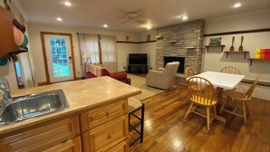 A modern kitchen with wooden cabinets, a sink, and a dining area with a white table and wooden chairs. - Clintonville Charmer | Walk to Great Restaurants! (Columbus)