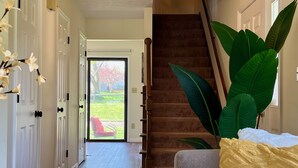 A hallway with a staircase, a door leading outside, and a large plant. - Westerville Comfort & Convenience (Westerville)