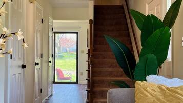 A hallway with a staircase, a door leading outside, and a large plant.