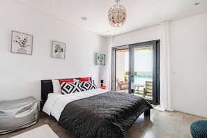 A bedroom with a bed, a bedside table, a chair, a bean bag, and a view of the sea through a sliding glass door. - BICA VISTA Boutique B&B (Lourinha)