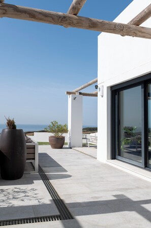 A modern outdoor patio with a view of the sea, featuring a wooden pergola, potted plants, and a seating area. - BICA VISTA Boutique B&B (Lourinha)