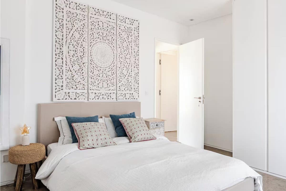 Une chambre à coucher moderne avec un grand lit, un panneau mural décoratif et une table de chevet avec une lampe.