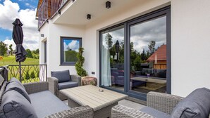 Un espace de vie extérieur moderne, avec des meubles en osier, une porte vitrée donnant sur un patio et une vue sur un quartier résidentiel.