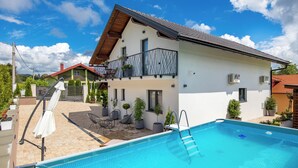 Une maison à deux étages avec une piscine, du mobilier d’extérieur et des plantes en pot.