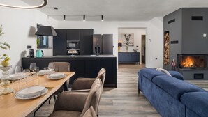 Un salon moderne avec un canapé bleu, une table à manger dressée avec des assiettes et des verres, une cuisine avec des meubles sombres et une cheminée.