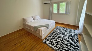 Une chambre à coucher avec un lit, un plancher en bois, une fenêtre avec des rideaux et un appareil de climatisation.