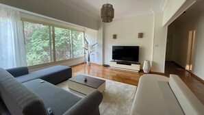 Un salon moderne doté d’une grande fenêtre, d’un téléviseur à écran plat et d’un canapé gris.