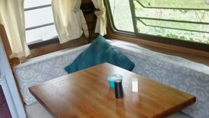 A compact, well-lit interior with a wooden table, a cushioned bench, and a window with curtains. - Cozy RV, cheap with priceless features. (Hector)