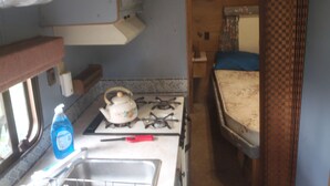 A compact kitchen with a gas stove, a sink, and a small window. - Cozy RV, cheap with priceless features. (Hector)