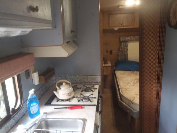 A compact kitchen with a gas stove, a sink, and a small window. - Cozy RV, cheap with priceless features. (Hector)