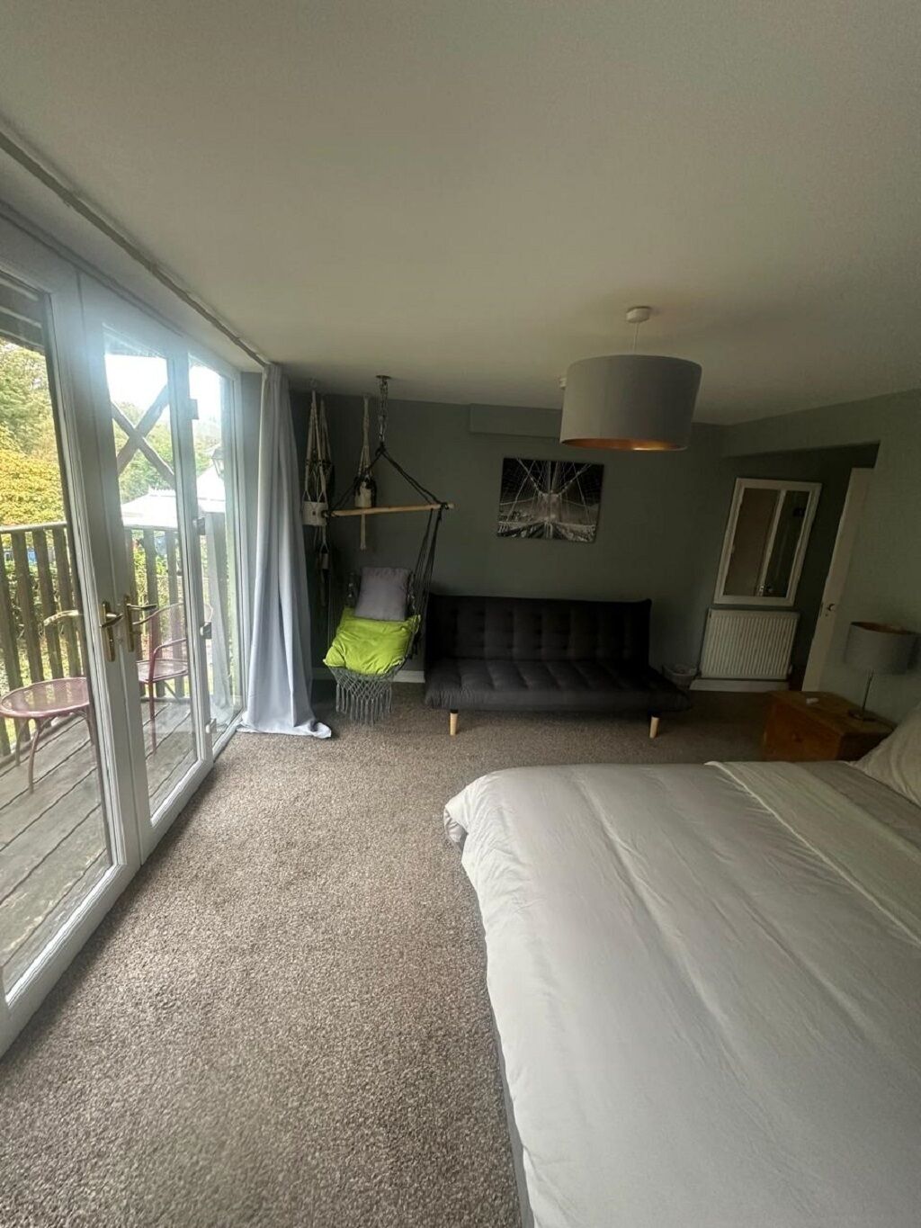 A bedroom with a large bed, a hanging chair, and a view of the outdoors through a sliding door.