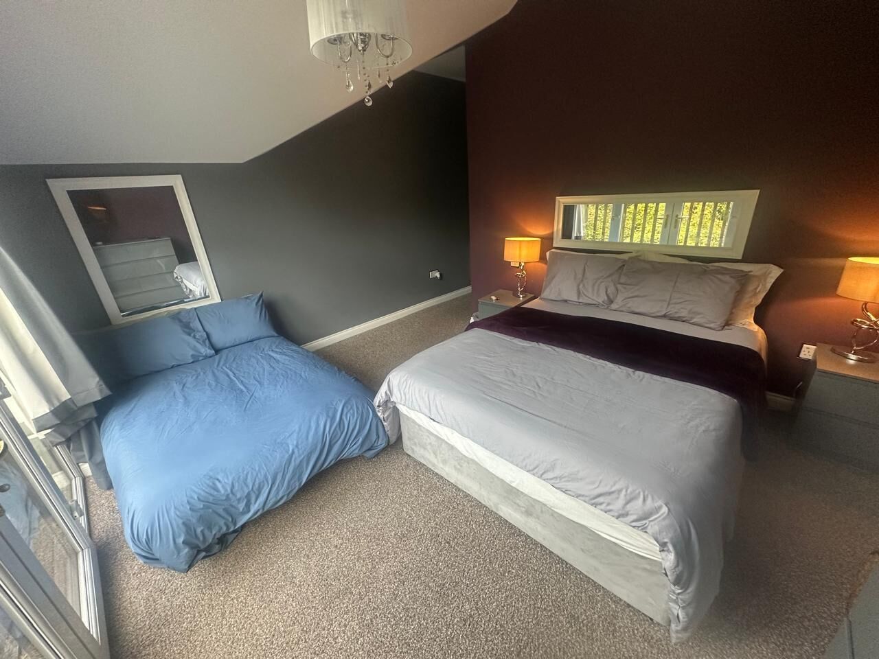 A bedroom with two beds, a large mirror, and a wall-mounted TV.