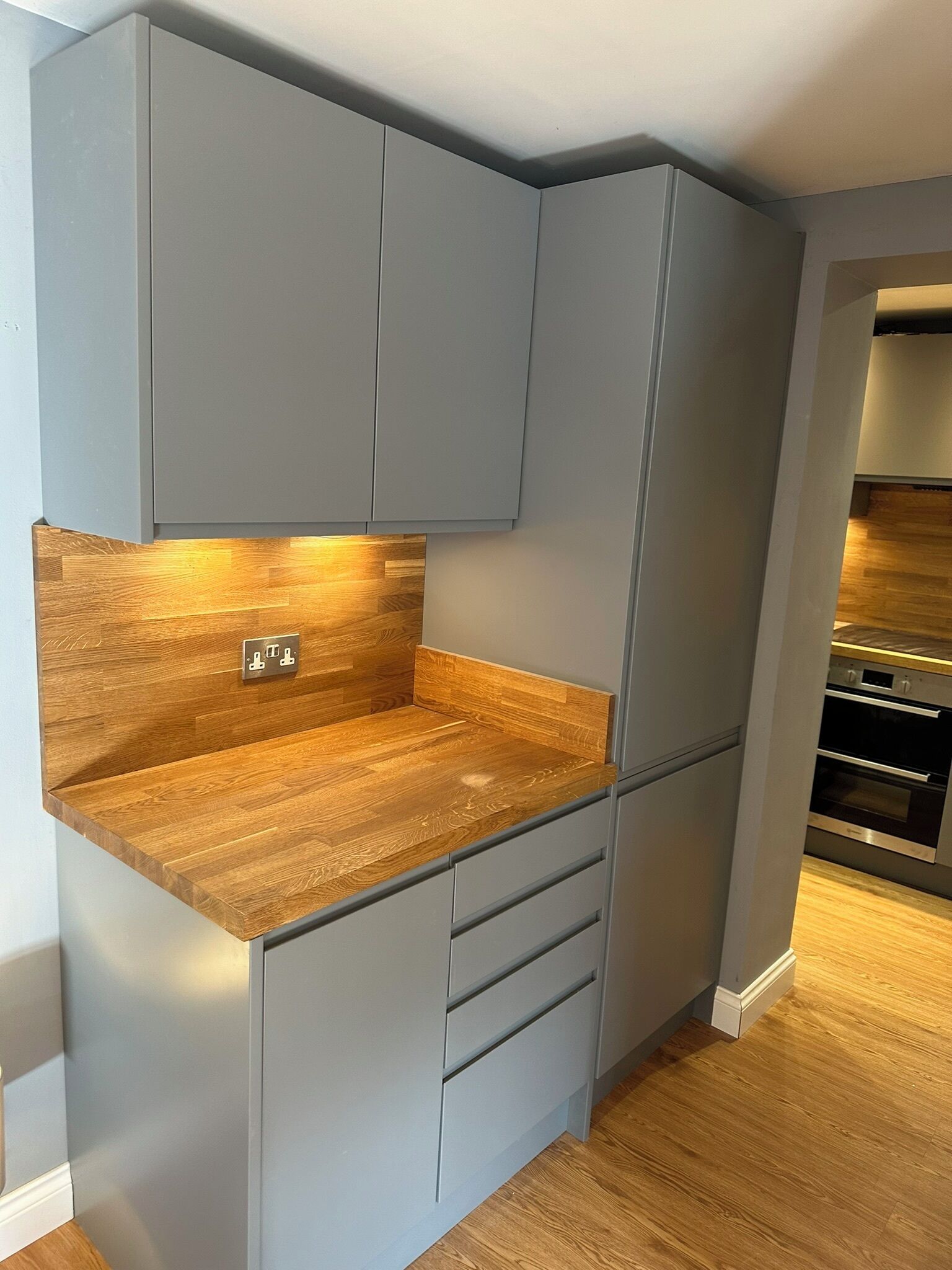 A compact kitchen with grey cabinets, a wooden countertop, and integrated appliances.