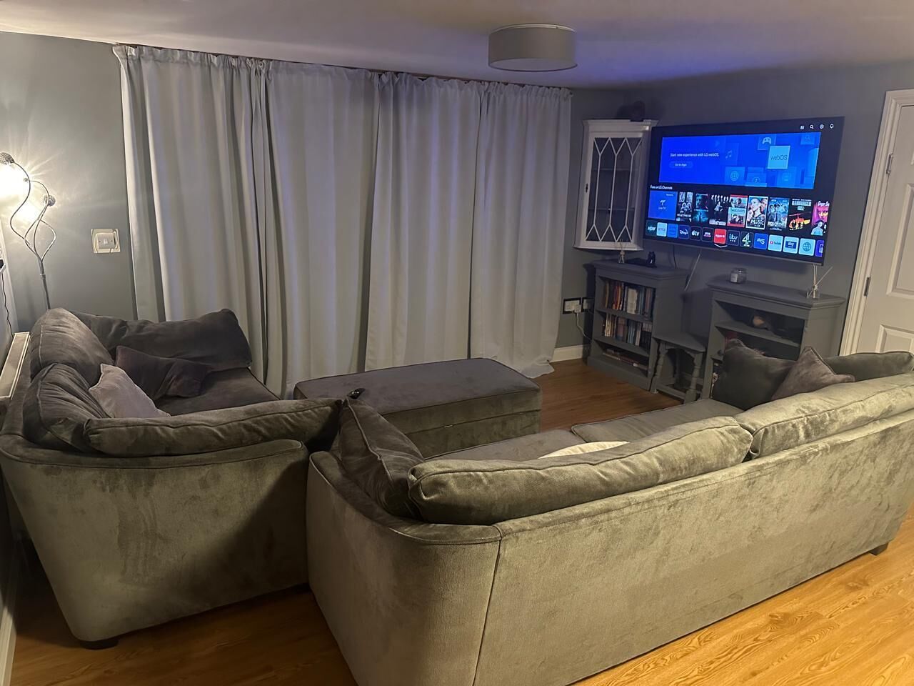 Een woonkamer met een grijze zithoek, een flatscreen televisie en een boekenkast.